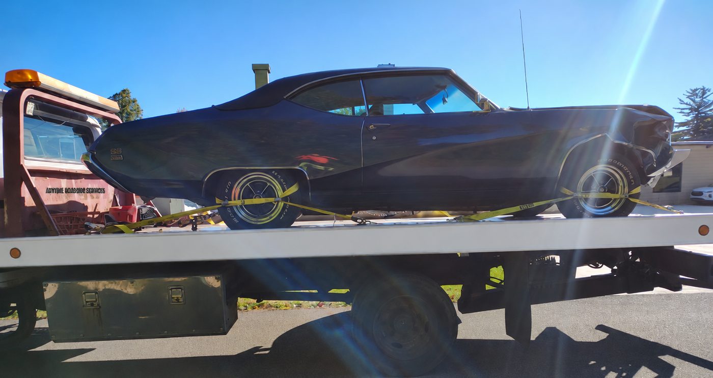 A classic car strapped down on the flatbed tow truck