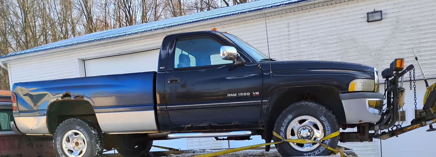 A pickup truck with a snowplow loaded and strapped on the flatbed