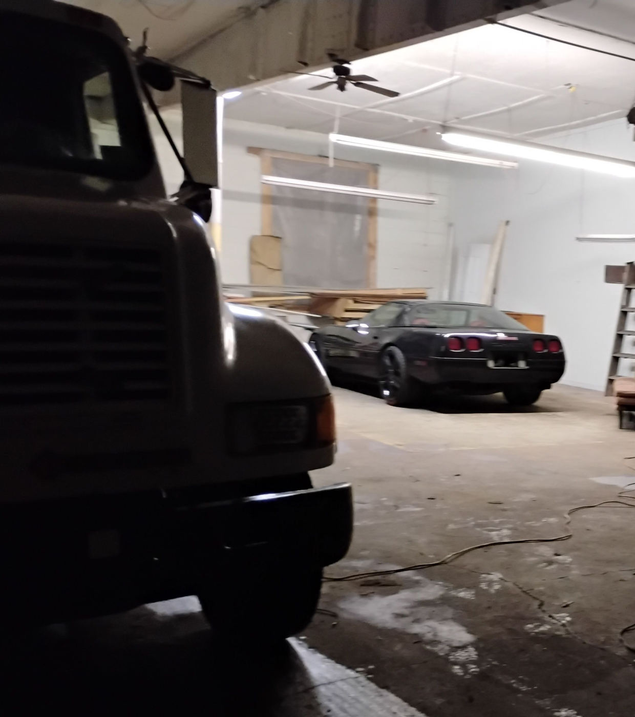 The front of the flatbed tow truck inside the shop, with a project car behind it