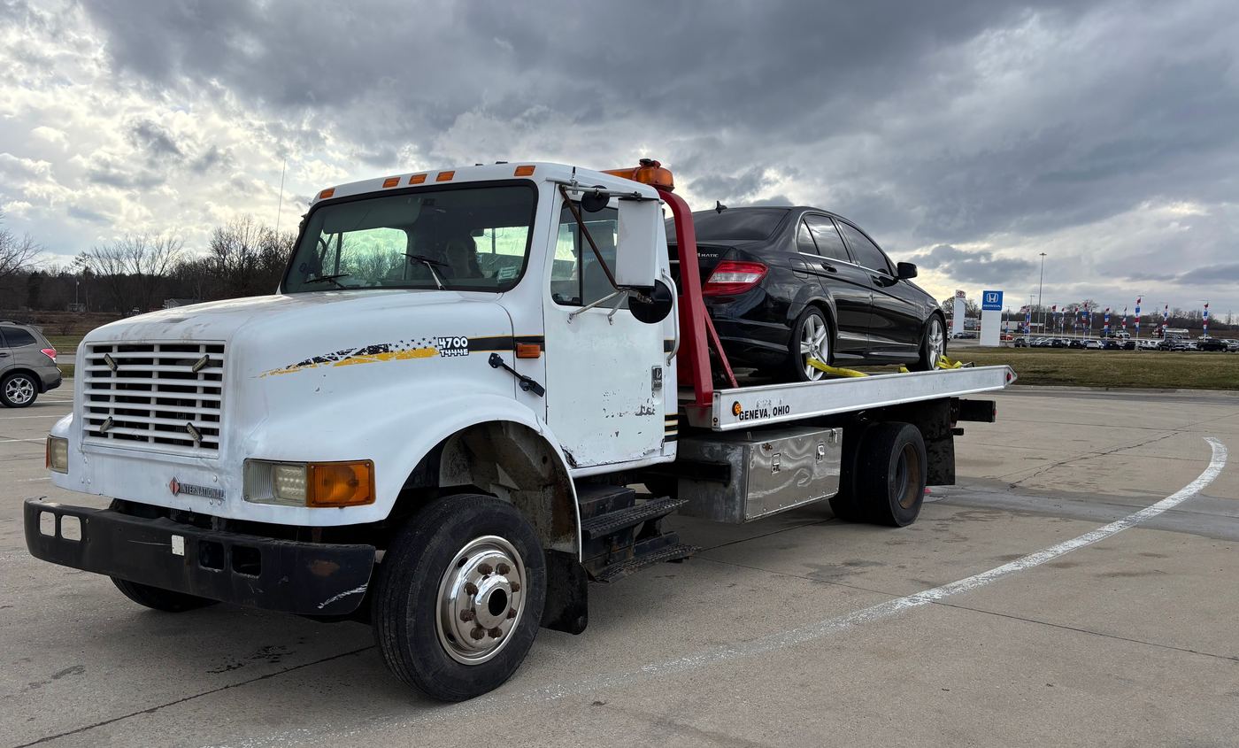 A black sedan loaded and strapped down on the deck of the Anytime Roadside Services flatbed